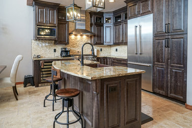 Mid-sized arts and crafts travertine floor and beige floor open concept kitchen photo in Denver with a farmhouse sink, raised-panel cabinets, dark wood cabinets, granite countertops, beige backsplash, stainless steel appliances and an island