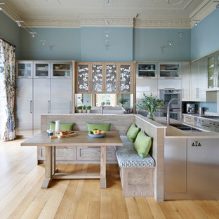 Photo of a large contemporary enclosed kitchen in Berkshire with a built-in sink, flat-panel cabinets, stainless steel cabinets, quartz worktops, beige splashback, stainless steel appliances, light hardwood flooring, an island and beige worktops.