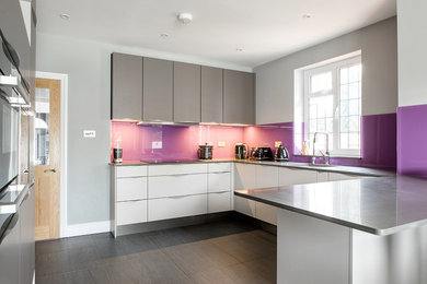 Photo of a medium sized contemporary u-shaped kitchen/diner in Surrey with a submerged sink, flat-panel cabinets, grey cabinets, quartz worktops, glass sheet splashback, integrated appliances, a breakfast bar and grey worktops.