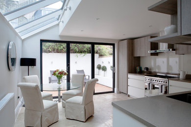 Photo of a large l-shaped kitchen/diner in London with white cabinets, granite worktops, stainless steel appliances, limestone flooring, no island, beige floors and grey worktops.