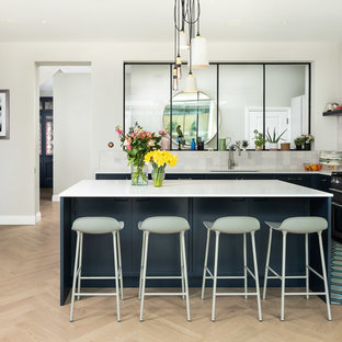 Design ideas for a contemporary l-shaped kitchen in London with a submerged sink, blue cabinets, grey splashback, stainless steel appliances, light hardwood flooring, an island, beige floors and white worktops.