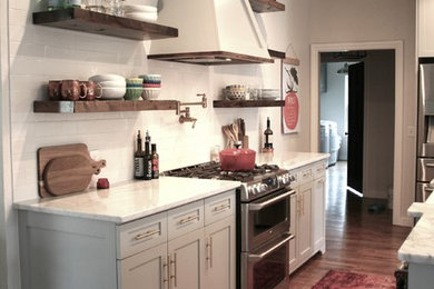 Mid-sized cottage l-shaped light wood floor and brown floor eat-in kitchen photo in Oklahoma City with a farmhouse sink, flat-panel cabinets, gray cabinets, marble countertops, white backsplash, subway tile backsplash, stainless steel appliances and an island