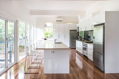 Einzeilige, Mittelgroße Moderne Wohnküche mit Einbauwaschbecken, flächenbündigen Schrankfronten, weißen Schränken, Marmor-Arbeitsplatte, Küchenrückwand in Weiß, Rückwand aus Keramikfliesen, weißen Elektrogeräten, dunklem Holzboden, Kücheninsel und braunem Boden in Brisbane