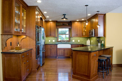 Bild på ett mellanstort amerikanskt kök, med en rustik diskho, skåp i shakerstil, skåp i mellenmörkt trä, granitbänkskiva, grönt stänkskydd, rostfria vitvaror, ljust trägolv och en halv köksö