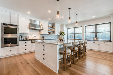 Example of a large classic u-shaped medium tone wood floor and brown floor open concept kitchen design in Bridgeport with recessed-panel cabinets, white cabinets, granite countertops, marble backsplash, stainless steel appliances, an island, gray countertops and a farmhouse sink