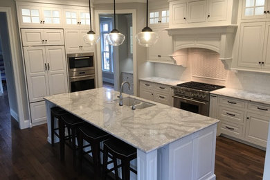 Example of a large transitional u-shaped dark wood floor and brown floor eat-in kitchen design in Other with a double-bowl sink, raised-panel cabinets, white cabinets, quartzite countertops, white backsplash, subway tile backsplash, stainless steel appliances and an island
