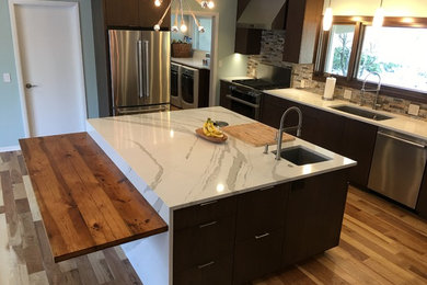 Example of a mid-sized trendy u-shaped medium tone wood floor and brown floor eat-in kitchen design in Other with a single-bowl sink, flat-panel cabinets, dark wood cabinets, quartzite countertops, gray backsplash, stone tile backsplash, stainless steel appliances and an island