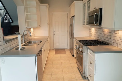 Galley kitchen photo in Toronto with an undermount sink, white cabinets, quartz countertops, white backsplash, stainless steel appliances, no island and gray countertops