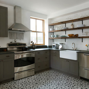This is an example of a mid-sized eclectic l-shaped eat-in kitchen in Philadelphia with a farmhouse sink, flat-panel cabinets, grey cabinets, white splashback, ceramic splashback, stainless steel appliances, porcelain floors, no island and multi-coloured floor.