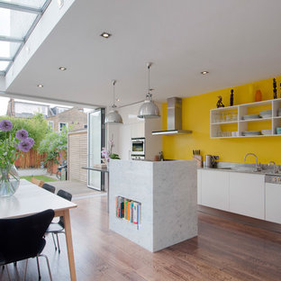 Inspiration for a contemporary kitchen/diner in London with an integrated sink, white cabinets, stainless steel worktops, yellow splashback, integrated appliances, dark hardwood flooring, an island, brown floors and open cabinets.