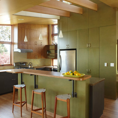 Example of a mid-sized trendy l-shaped medium tone wood floor and brown floor open concept kitchen design in San Francisco with flat-panel cabinets, green cabinets, green backsplash, stainless steel appliances, wood countertops, glass tile backsplash and an island
