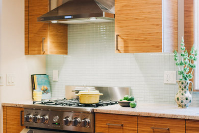 Modern inredning av ett mellanstort kök, med en halv köksö, släta luckor, skåp i ljust trä, granitbänkskiva, grönt stänkskydd, stänkskydd i glaskakel, rostfria vitvaror, en undermonterad diskho och ljust trägolv