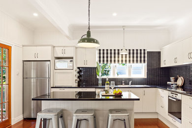 Bild på ett amerikanskt kök, med en dubbel diskho, granitbänkskiva, svart stänkskydd, rostfria vitvaror, ljust trägolv och en köksö