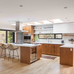 Ispirazione per una cucina a L minimalista con lavello sottopiano, ante lisce, ante in legno scuro, paraspruzzi bianco, elettrodomestici in acciaio inossidabile, parquet chiaro, isola, pavimento beige e top bianco