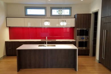 Kitchen - mid-sized contemporary l-shaped light wood floor kitchen idea in Denver with an undermount sink, flat-panel cabinets, dark wood cabinets, solid surface countertops, red backsplash, glass sheet backsplash, paneled appliances, an island and white countertops