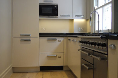 Inspiration for a small modern l-shaped enclosed kitchen in London with a double-bowl sink, flat-panel cabinets, white cabinets, granite worktops, integrated appliances, light hardwood flooring and no island.