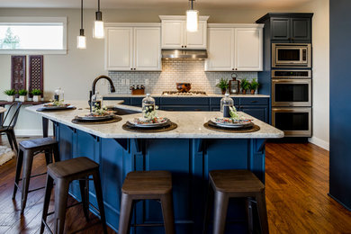 Example of a mid-sized transitional medium tone wood floor kitchen design in Portland with raised-panel cabinets, blue cabinets, quartzite countertops, subway tile backsplash, stainless steel appliances and an island