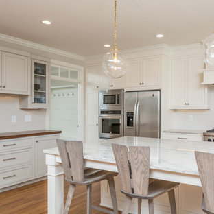 Large transitional eat-in kitchen pictures - Inspiration for a large transitional u-shaped medium tone wood floor and brown floor eat-in kitchen remodel in Raleigh with a farmhouse sink, shaker cabinets, white cabinets, white backsplash, stainless steel appliances, an island, quartzite countertops, subway tile backsplash and white countertops