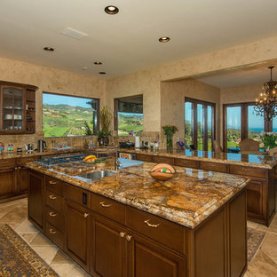 This is an example of a mid-sized mediterranean u-shaped separate kitchen in Los Angeles with a double-bowl sink, raised-panel cabinets, dark wood cabinets, granite benchtops, multi-coloured splashback, stone tile splashback, stainless steel appliances, ceramic floors, multiple islands, brown floor and brown benchtop.