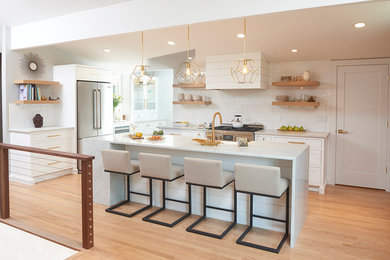 Example of a mid-sized transitional l-shaped medium tone wood floor kitchen design in New York with a farmhouse sink, shaker cabinets, white cabinets, marble countertops, white backsplash, subway tile backsplash, stainless steel appliances and an island