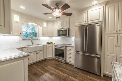 Mid-sized elegant u-shaped dark wood floor and brown floor enclosed kitchen photo in Kansas City with a farmhouse sink, raised-panel cabinets, white cabinets, granite countertops, white backsplash, subway tile backsplash, stainless steel appliances and no island