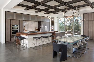 Example of a trendy galley concrete floor and gray floor open concept kitchen design in San Diego with a double-bowl sink, flat-panel cabinets, medium tone wood cabinets, quartz countertops, white backsplash, stainless steel appliances, an island and ceramic backsplash