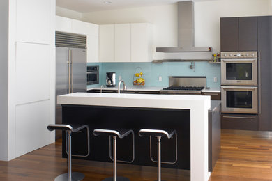 Design ideas for a large modern l-shaped kitchen in San Francisco with flat-panel cabinets, blue splashback, glass sheet splashback, stainless steel appliances, dark hardwood flooring, an island, brown floors, a submerged sink, white cabinets and engineered stone countertops.