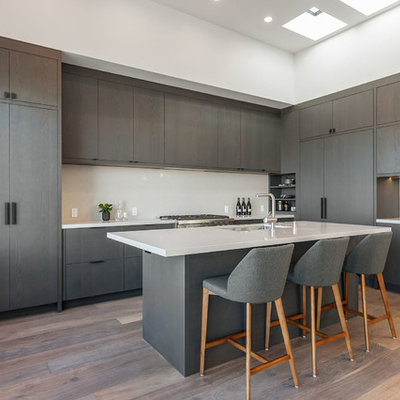Trendy l-shaped brown floor and medium tone wood floor kitchen photo in San Francisco with an undermount sink, flat-panel cabinets, gray cabinets, white backsplash, paneled appliances, an island and white countertops