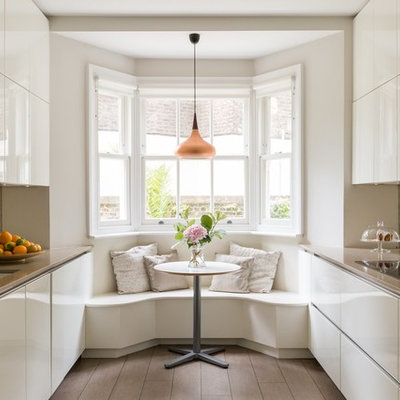 Eat-in kitchen - mid-sized contemporary galley brown floor and dark wood floor eat-in kitchen idea in London with flat-panel cabinets, white cabinets, mirror backsplash, beige countertops, an undermount sink, metallic backsplash, paneled appliances and no island