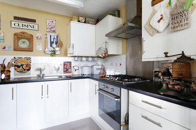 ロンドンにある小さなシャビーシック調のおしゃれなキッチン (ドロップインシンク、フラットパネル扉のキャビネット、白いキャビネット、ラミネートカウンター、メタリックのキッチンパネル、シルバーの調理設備、アイランドなし、グレーの床) の写真