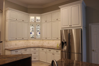 Large elegant u-shaped porcelain tile and beige floor enclosed kitchen photo in Jacksonville with white cabinets, a double-bowl sink, raised-panel cabinets, granite countertops, beige backsplash, porcelain backsplash, stainless steel appliances, an island and multicolored countertops