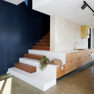 This is an example of a mid-sized contemporary galley kitchen in Adelaide with a double-bowl sink, flat-panel cabinets, medium wood cabinets, quartz benchtops, white splashback, brick splashback, stainless steel appliances, concrete floors, grey floor and white benchtop.