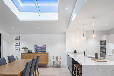 Photo of a large contemporary galley kitchen/diner in Dublin with a submerged sink, flat-panel cabinets, white cabinets, granite worktops, light hardwood flooring, an island, grey floors and stainless steel appliances.
