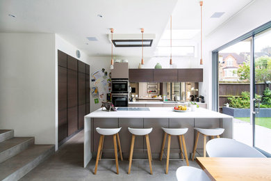This is an example of a medium sized contemporary l-shaped kitchen/diner in London with a submerged sink, flat-panel cabinets, dark wood cabinets, mirror splashback, an island, grey floors and concrete flooring.