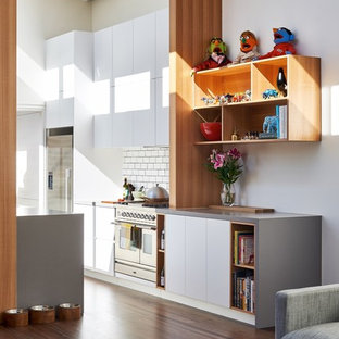Photo of a contemporary galley open plan kitchen in Sydney with flat-panel cabinets, white cabinets, white splashback, subway tile splashback, stainless steel appliances, dark hardwood floors and grey benchtop.