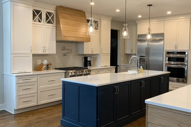 Large transitional galley medium tone wood floor and brown floor open concept kitchen photo in Detroit with a farmhouse sink, flat-panel cabinets, white cabinets, quartz countertops, white backsplash, porcelain backsplash, stainless steel appliances, two islands and white countertops