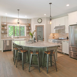 Example of a mid-sized arts and crafts l-shaped medium tone wood floor and brown floor open concept kitchen design in Portland Maine with a farmhouse sink, beaded inset cabinets, white cabinets, granite countertops, beige backsplash, stone tile backsplash, stainless steel appliances and an island