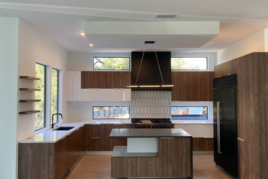 Inspiration for a large modern concrete floor open concept kitchen remodel in Austin with an undermount sink, flat-panel cabinets, medium tone wood cabinets, quartz countertops, white backsplash, black appliances, an island and black countertops