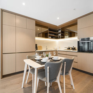Photo of a contemporary open plan kitchen in Sydney with an undermount sink, flat-panel cabinets, brown cabinets, white splashback, panelled appliances, medium hardwood floors, no island, brown floor and white benchtop.