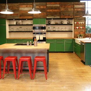 Industrial open concept kitchen ideas - Urban u-shaped open concept kitchen photo in Portland with a farmhouse sink, flat-panel cabinets, green cabinets, wood countertops, beige backsplash, subway tile backsplash and stainless steel appliances