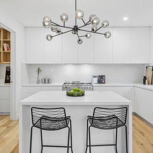 Photo of a small contemporary l-shaped eat-in kitchen in Melbourne with white cabinets, quartz benchtops, white splashback, marble splashback, stainless steel appliances, light hardwood floors, with island, white benchtop, a double-bowl sink, flat-panel cabinets and beige floor.
