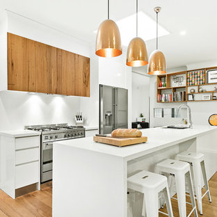 This is an example of a mid-sized contemporary galley open plan kitchen in Melbourne with an undermount sink, flat-panel cabinets, white cabinets, quartz benchtops, white splashback, stainless steel appliances, medium hardwood floors, with island, white benchtop and beige floor.