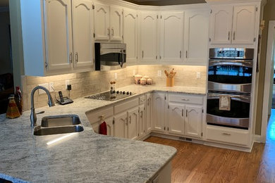 Inspiration for a mid-sized timeless l-shaped medium tone wood floor eat-in kitchen remodel in Other with an undermount sink, recessed-panel cabinets, white cabinets, granite countertops, porcelain backsplash and stainless steel appliances