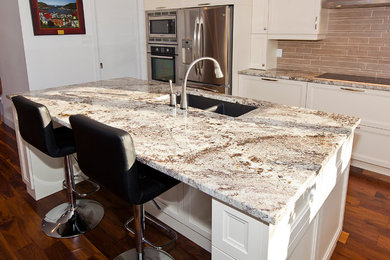 Example of a mid-sized trendy l-shaped medium tone wood floor kitchen design in Montreal with a double-bowl sink, shaker cabinets, white cabinets, granite countertops, beige backsplash, stone tile backsplash, stainless steel appliances and an island