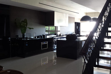 Example of a large minimalist galley porcelain tile and white floor eat-in kitchen design in San Diego with flat-panel cabinets, black cabinets, solid surface countertops, black backsplash, stone slab backsplash, stainless steel appliances and an island