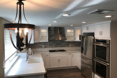 Inspiration for a mid-sized transitional u-shaped dark wood floor and brown floor kitchen remodel in San Diego with a farmhouse sink, shaker cabinets, white cabinets, quartz countertops, gray backsplash, porcelain backsplash, stainless steel appliances and no island