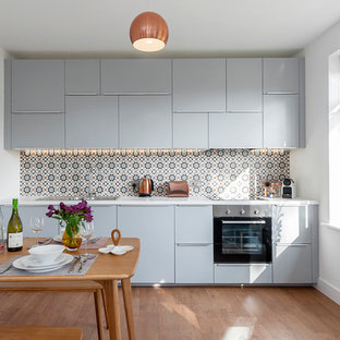 Small contemporary single-wall kitchen/diner in Wiltshire with flat-panel cabinets, blue cabinets, stainless steel appliances, light hardwood flooring, brown floors, a built-in sink and multi-coloured splashback.