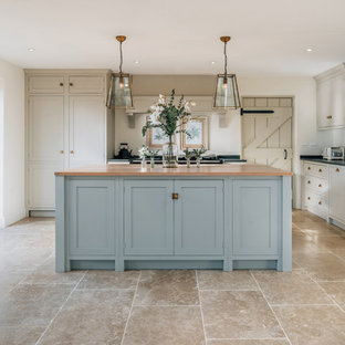 Photo of a medium sized traditional l-shaped kitchen/diner in Cambridgeshire with a belfast sink, shaker cabinets, black appliances, an island, brown floors and beige cabinets.