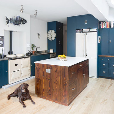 Elegant light wood floor and beige floor kitchen photo in London with an integrated sink, blue cabinets, stainless steel countertops, white appliances and an island