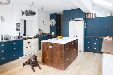 ロンドンにあるトラディショナルスタイルのおしゃれなアイランドキッチン (一体型シンク、青いキャビネット、ステンレスカウンター、白い調理設備、淡色無垢フローリング、ベージュの床) の写真